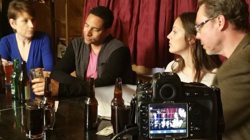 Photo of four actors shooting a scene at a bar.