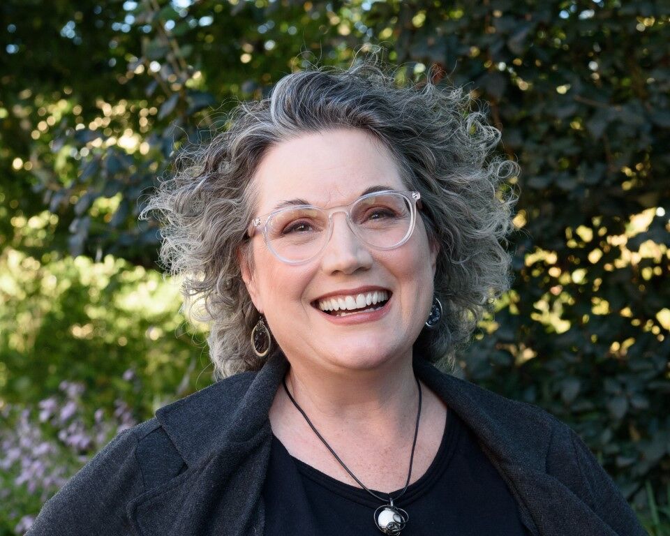 Photo of laughing woman with glasses and curly gray windblown hair.